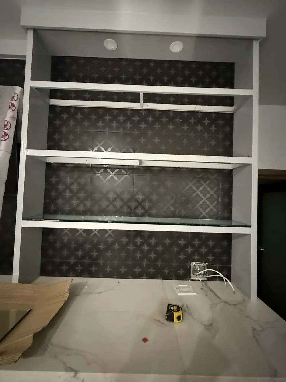 Plate glass shelves fitted into a wall niche backed with dark patterned tile.