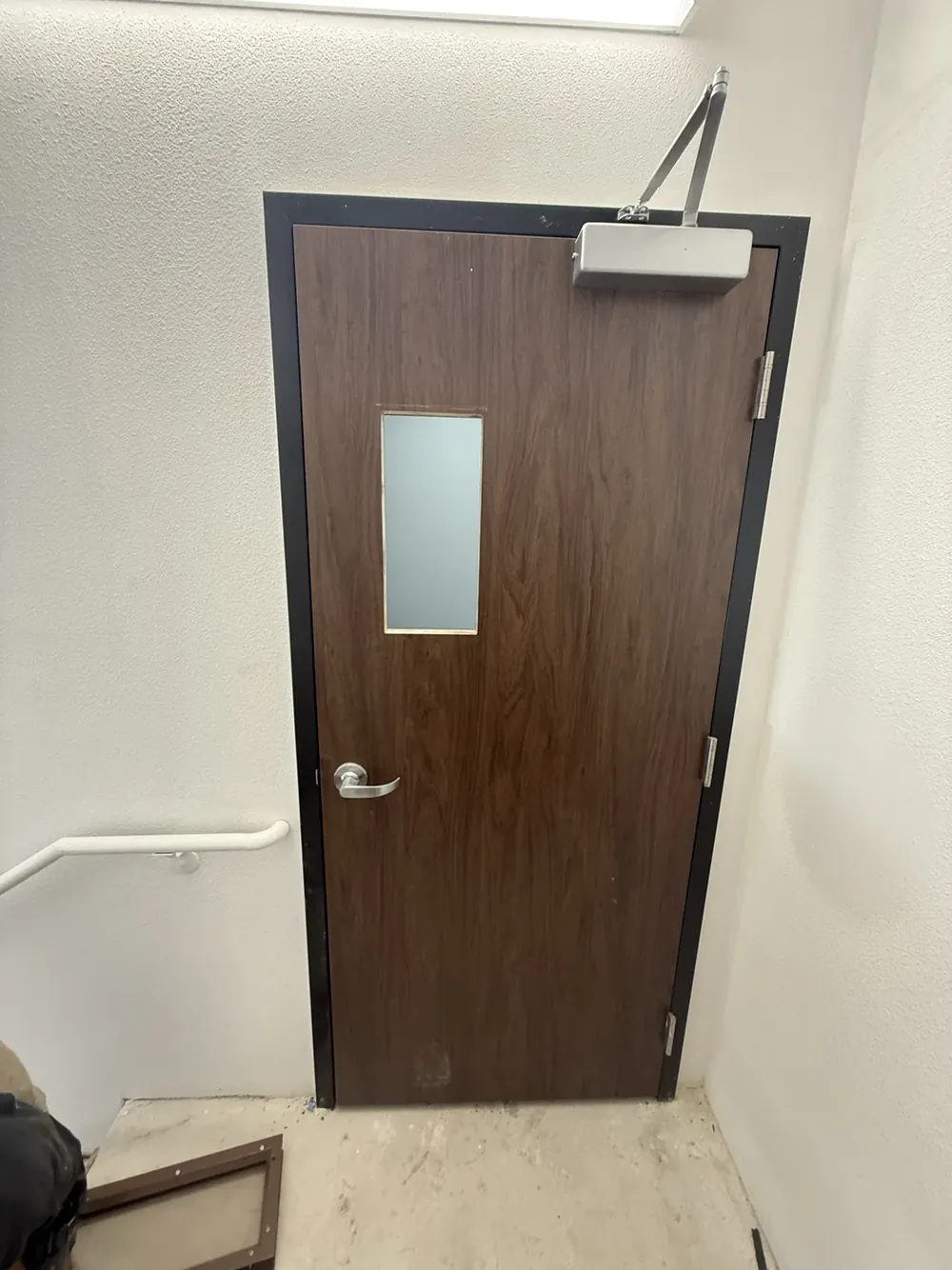 A wood entry door with a vision glass panel and overhead closer.