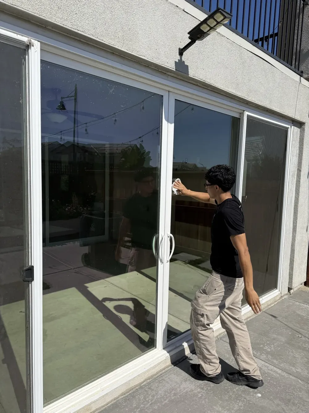 A person fitting a large black-framed sliding glass door panel on a home exterior.