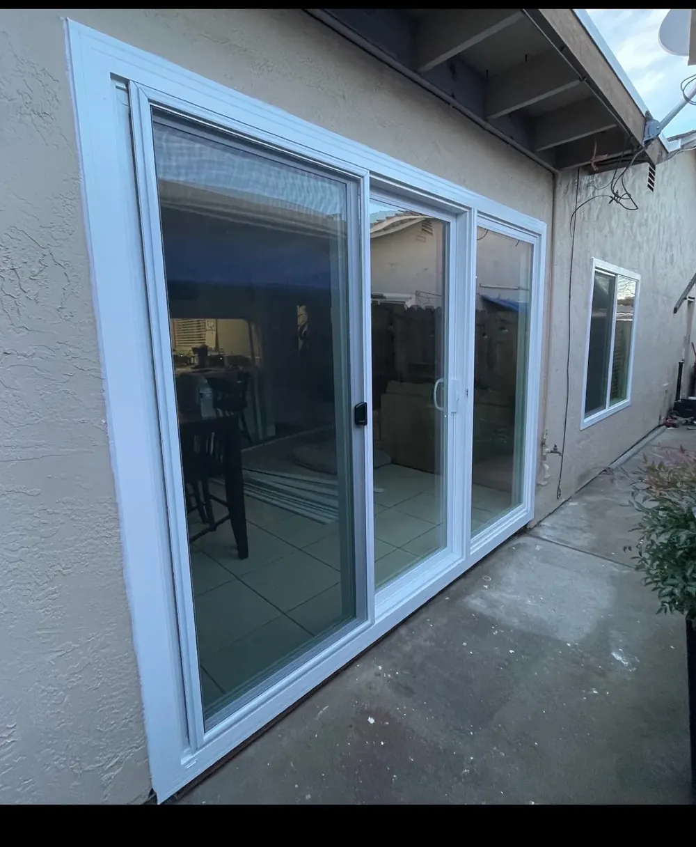 White-framed triple sliding glass patio doors along the side of a house.