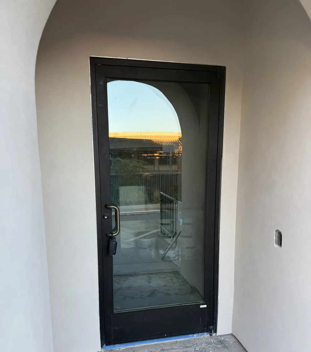A black-framed entry door with a full glass lite set into an arched stucco opening.