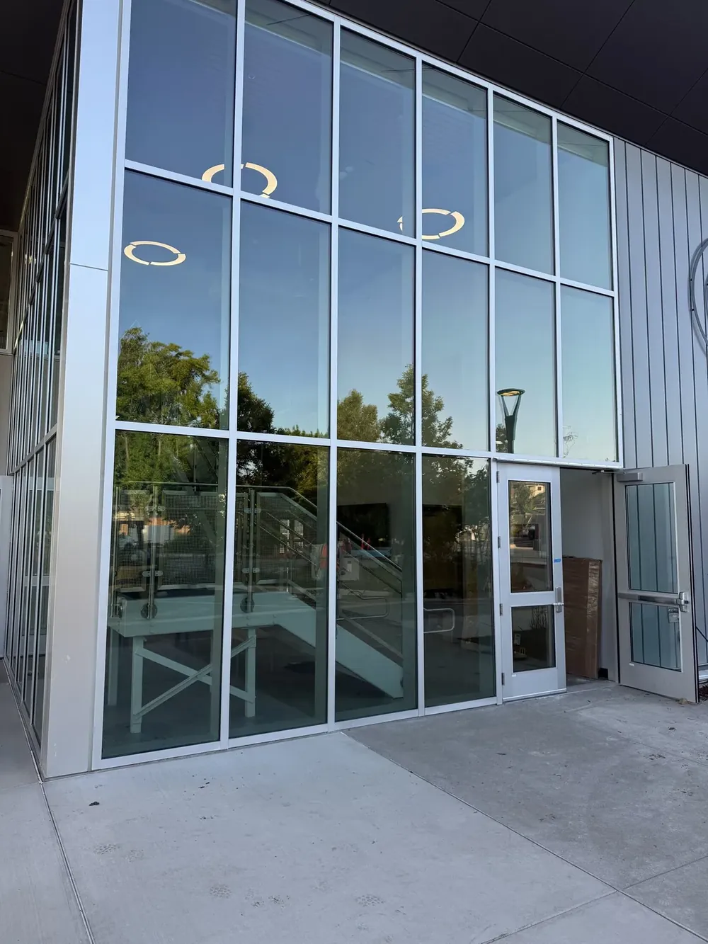 A finished commercial glass facade with aluminium framing and an entrance door reflecting the evening sky.