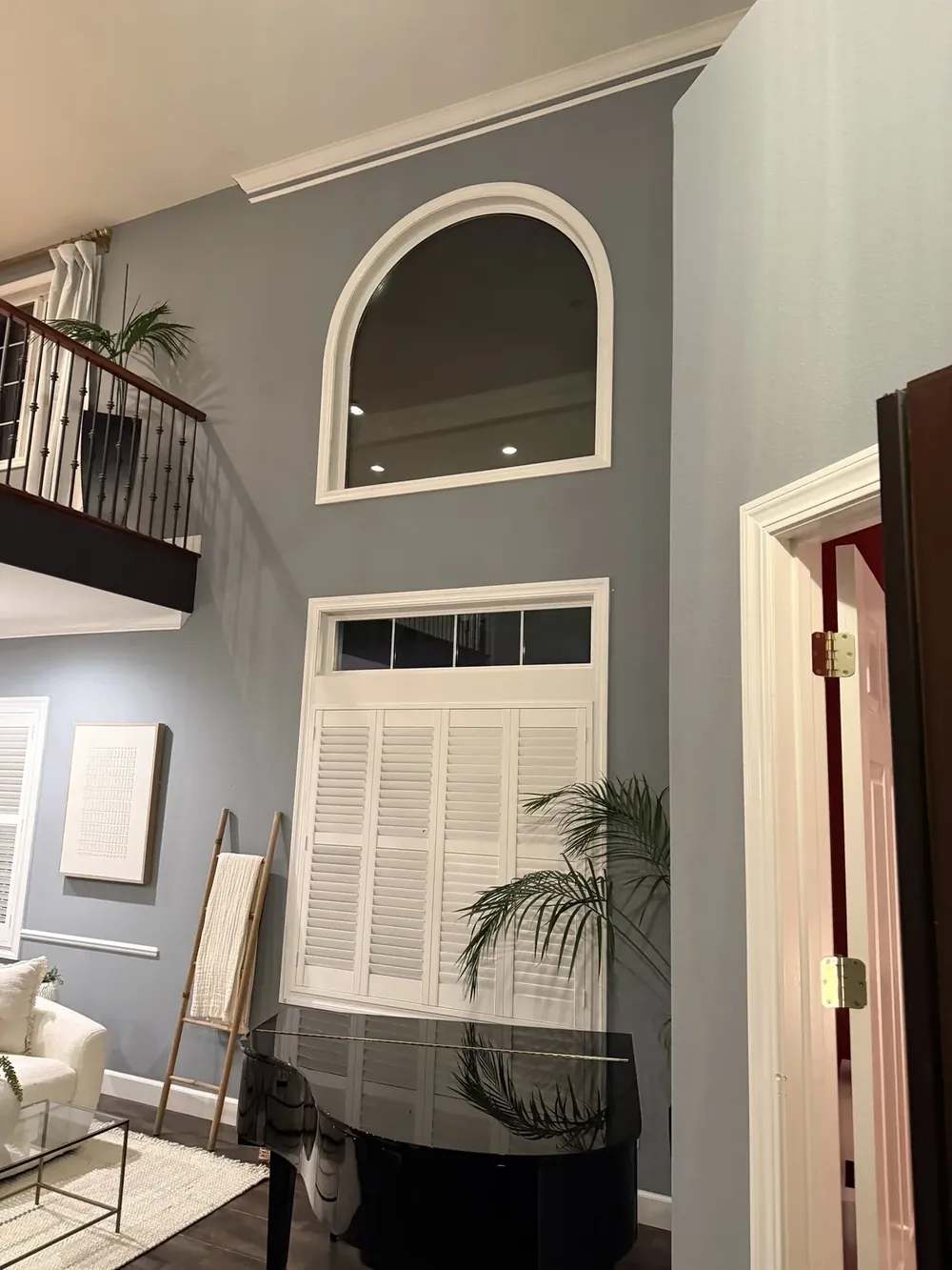 An arched window above a shuttered window in a two-storey living room.