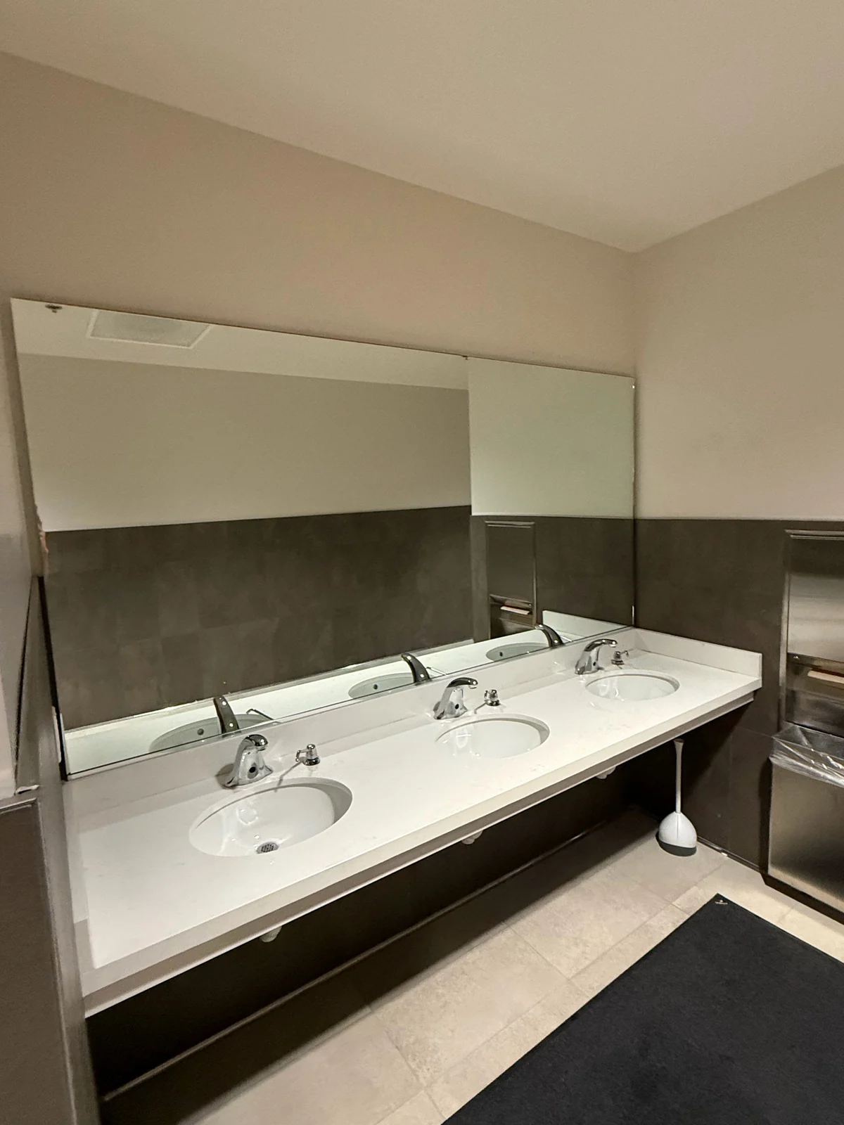 A large custom wall mirror above a white three-basin vanity in a tiled restroom.