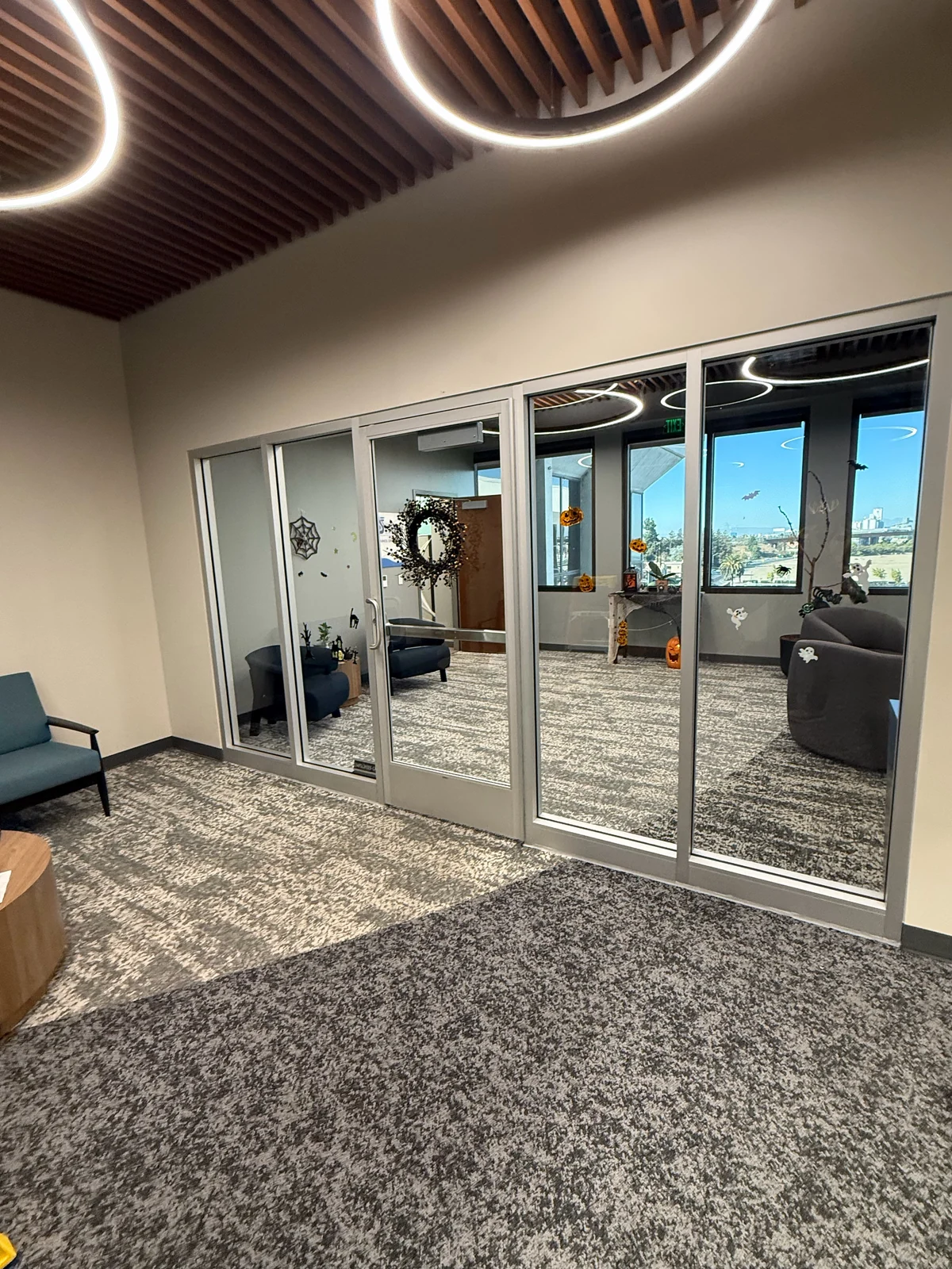 An aluminium-framed glass entrance with a door and sidelights in a furnished lobby.